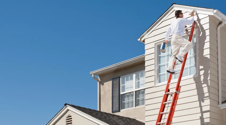 Professional painter applying exterior paint to a home in mild weather conditions
