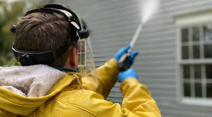 Professional power washing a home’s exterior surface before painting